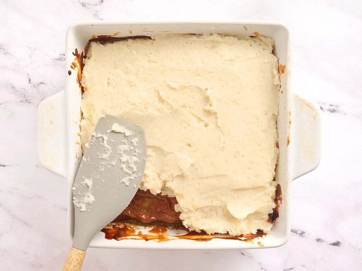 Purée de pommes de terre étalée sur une cocotte de pain de viande dans un plat allant au four.