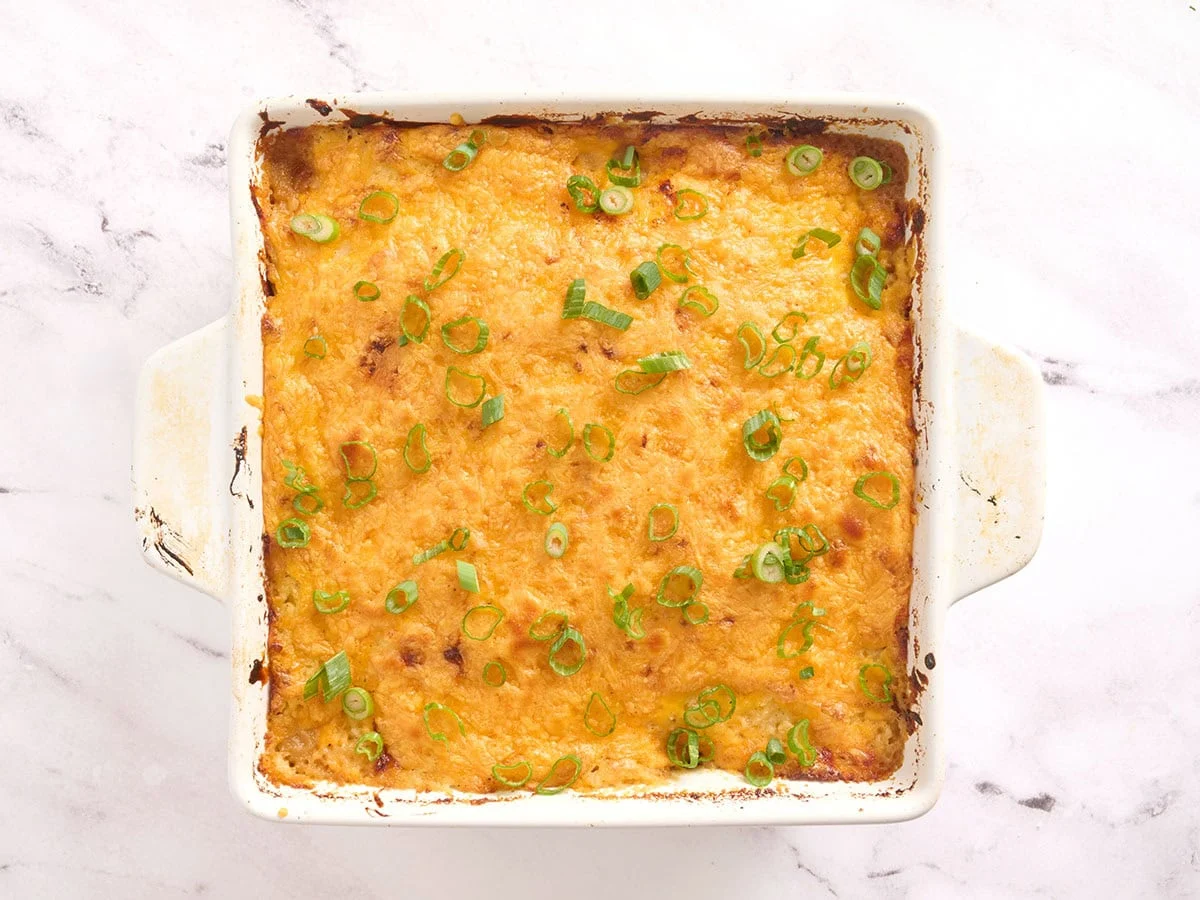 Casserole de pain de viande après cuisson au four, recouverte de fromage fondu et d'oignons verts émincés.
