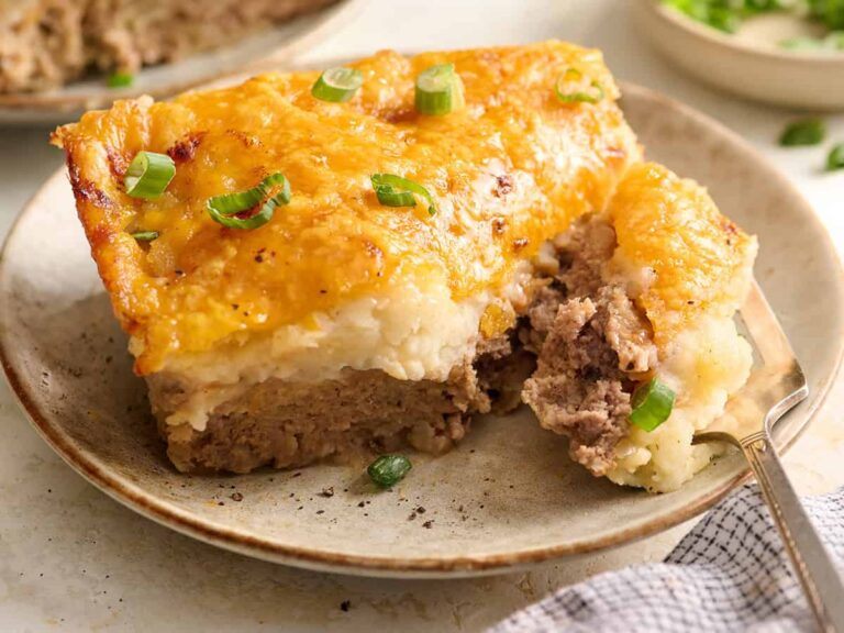 Side view of a slice of meatloaf casserole on a plate with a fork.