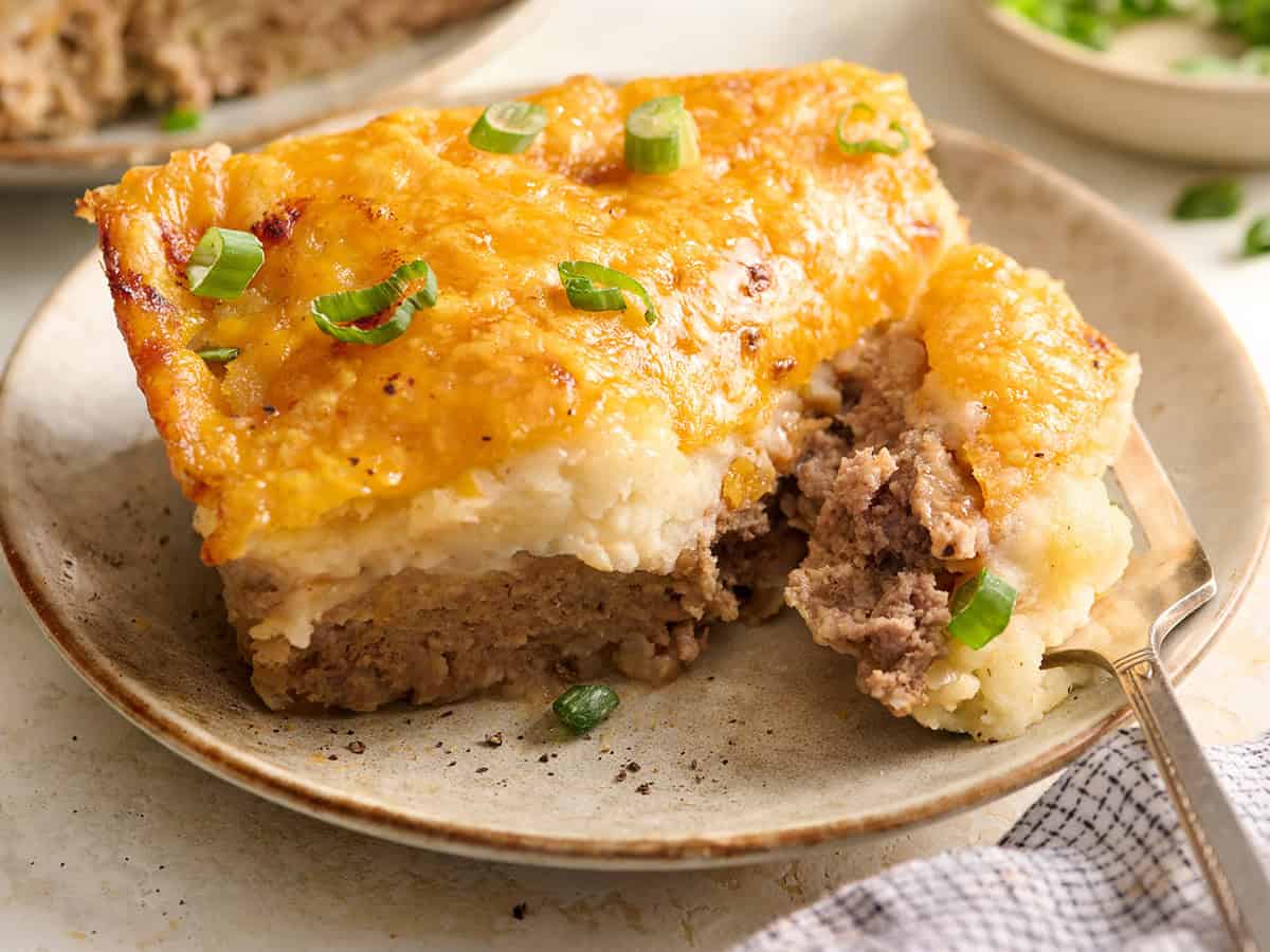 Side view of a slice of meatloaf casserole on a plate with a fork.
