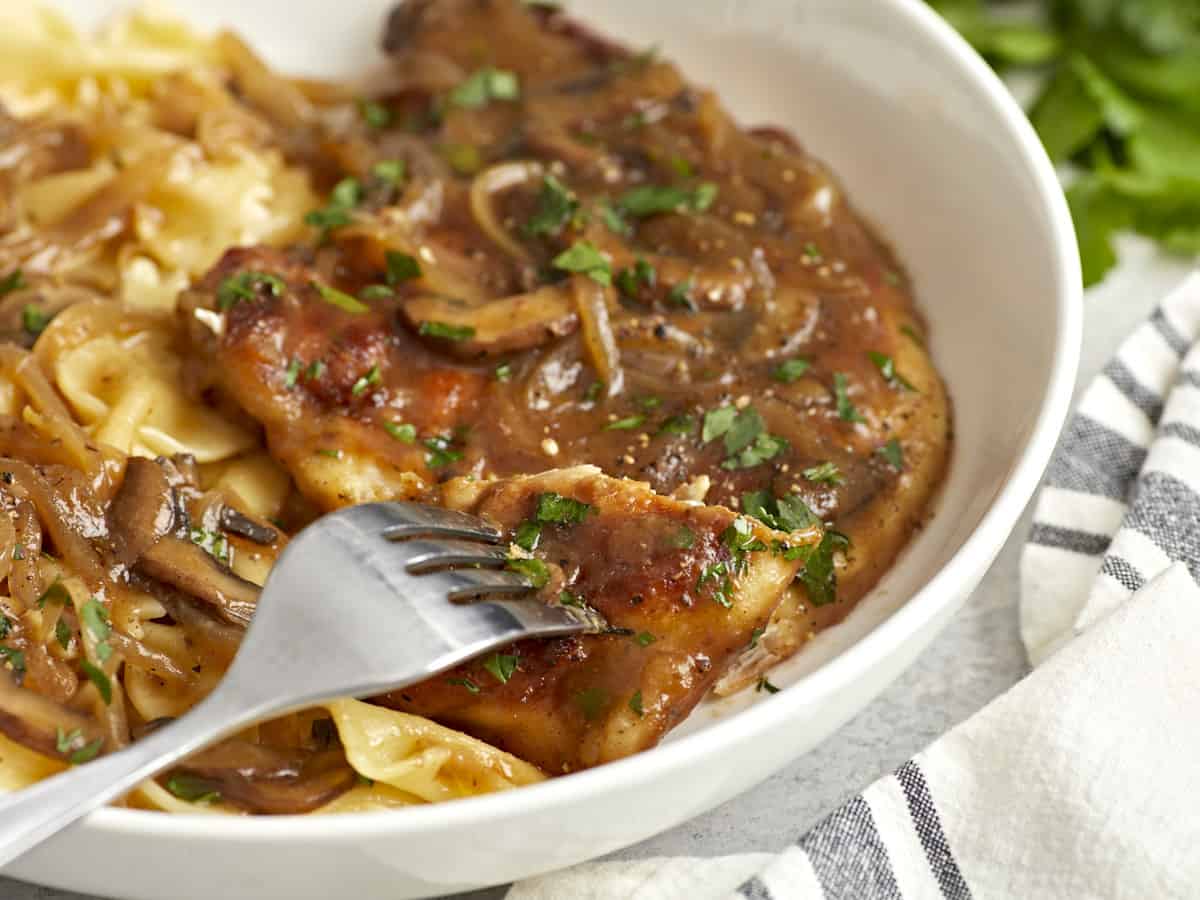 une fourchette tenant un morceau de poulet marsala au-dessus d'un plat peu profond.