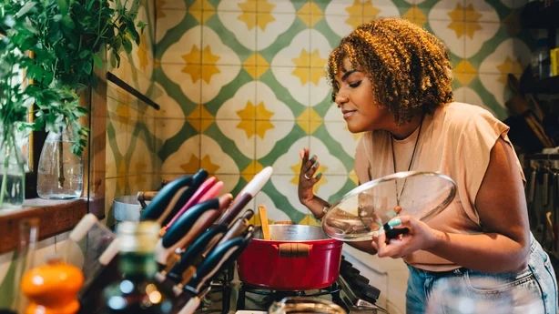 Femme souriant les yeux fermés tout en sentant la nourriture cuisinant dans une casserole sur une cuisinière dans sa cuisine à la maison