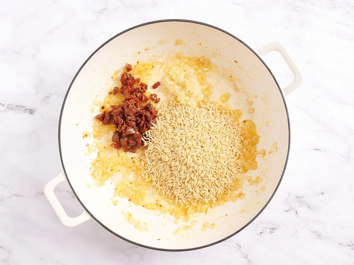 Orzo, tomates séchées en dés et ail dans une poêle.