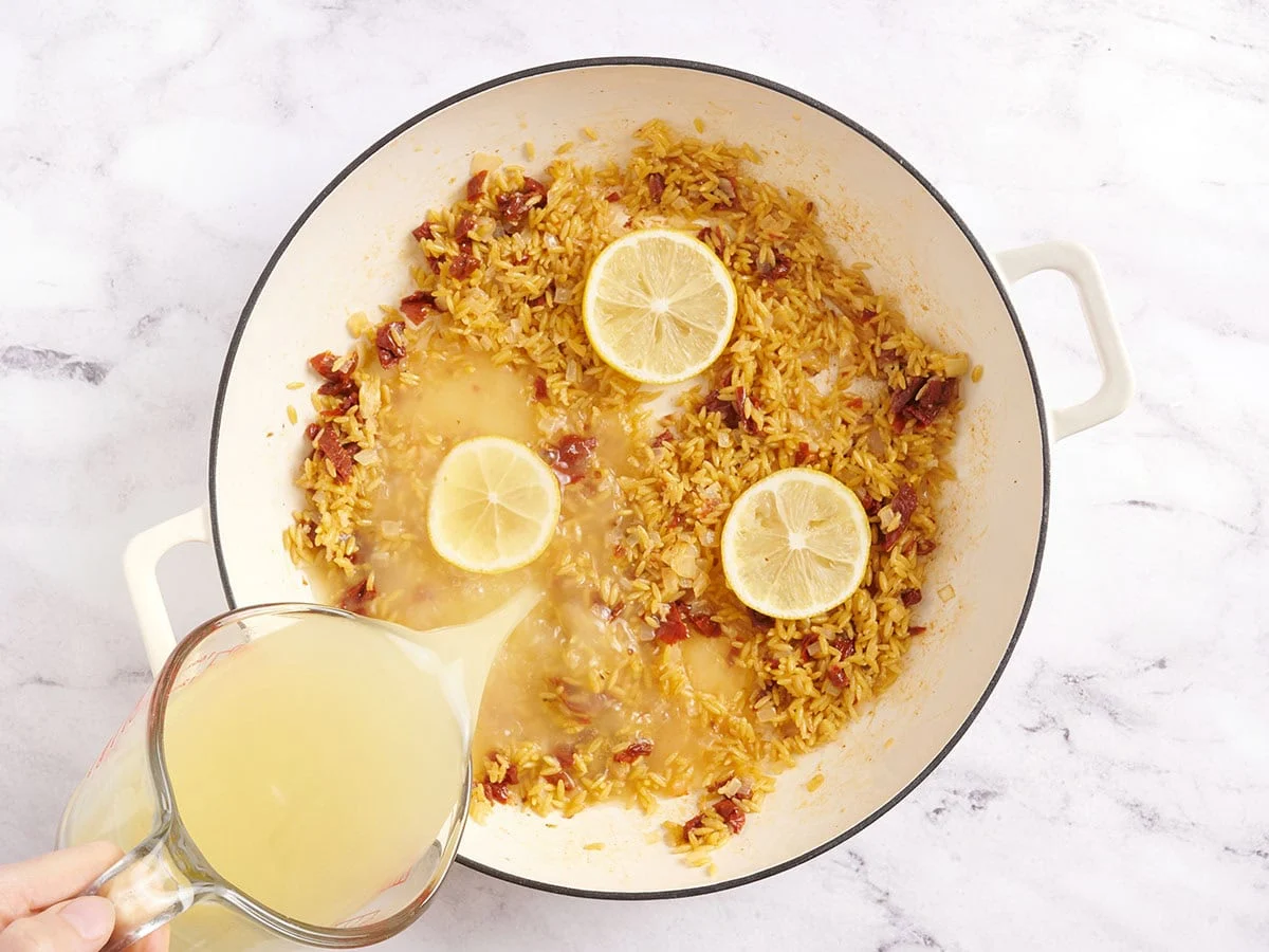 Tranches de citron et oignons dans une poêle avec du bouillon de poulet versé.