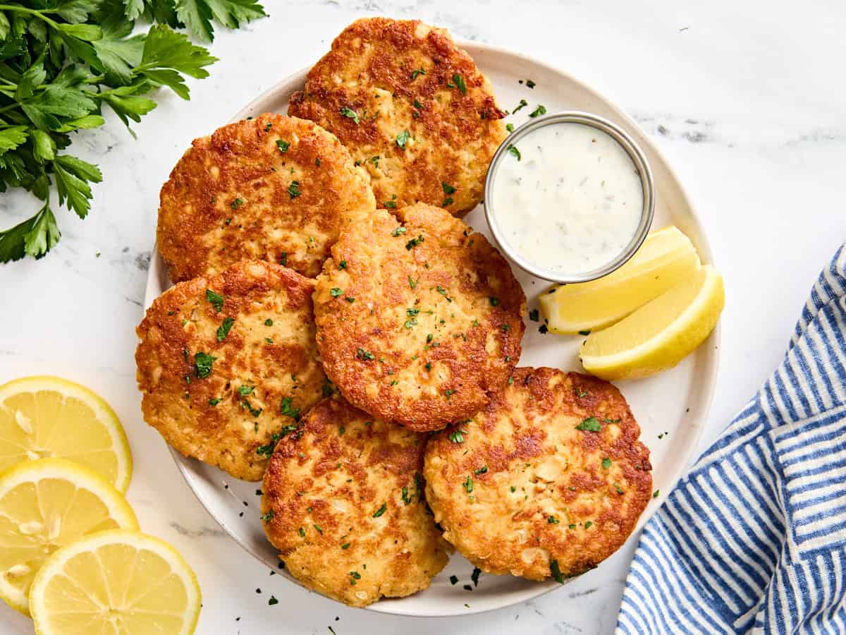 Vue aérienne de galettes de saumon maison sur une assiette avec sauce tartare et quartiers de citron.
