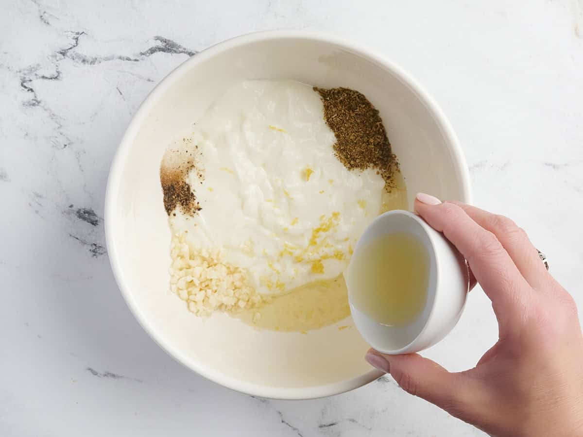 Le jus de citron est versé dans un bol de yaourt, d'ail et d'herbes.