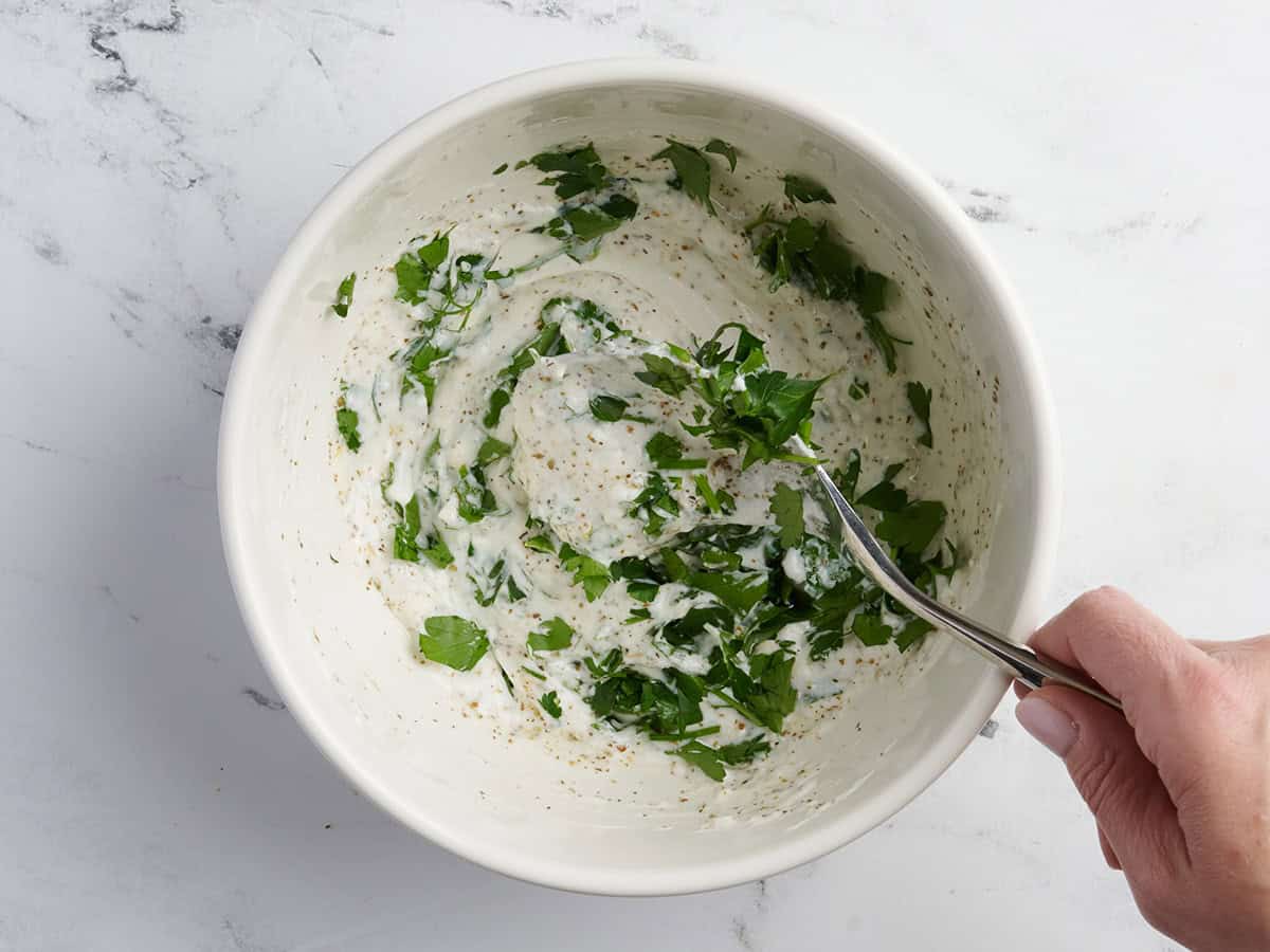 Persil ajouté à un bol de marinade de poulet à la grecque.