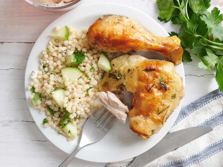 Overhead view of a plate of greek marinated chicken with couscous and a fork with some chicken on.