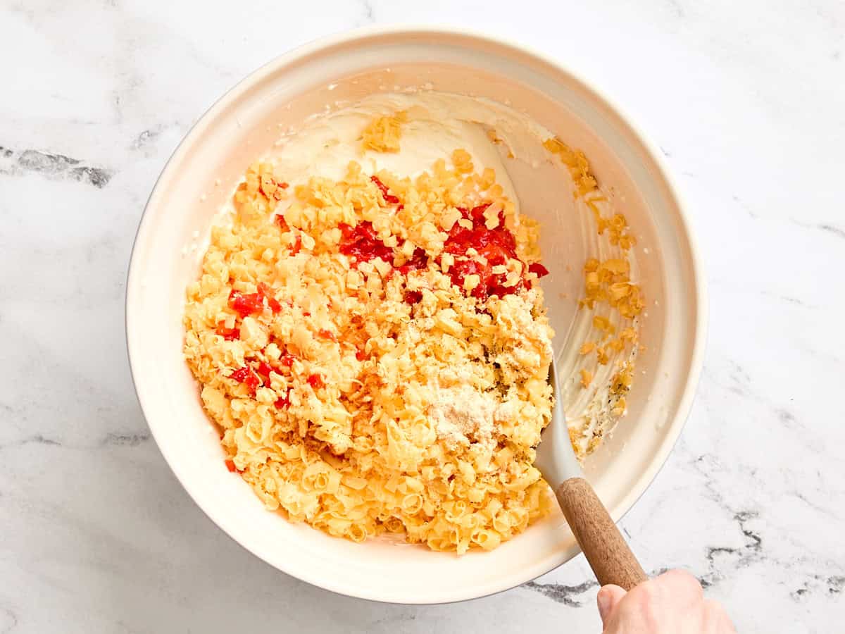 Du cheddar râpé et des piments émincés s'ajoutent à un bol de mayonnaise et de fromage à la crème combinés.