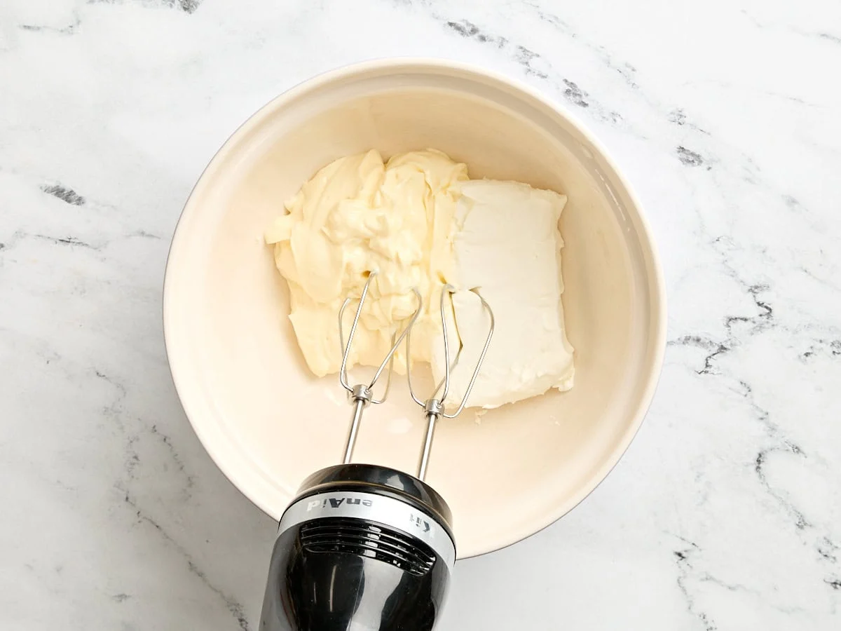 Mayo et fromage à la crème dans un bol avec un batteur à main.