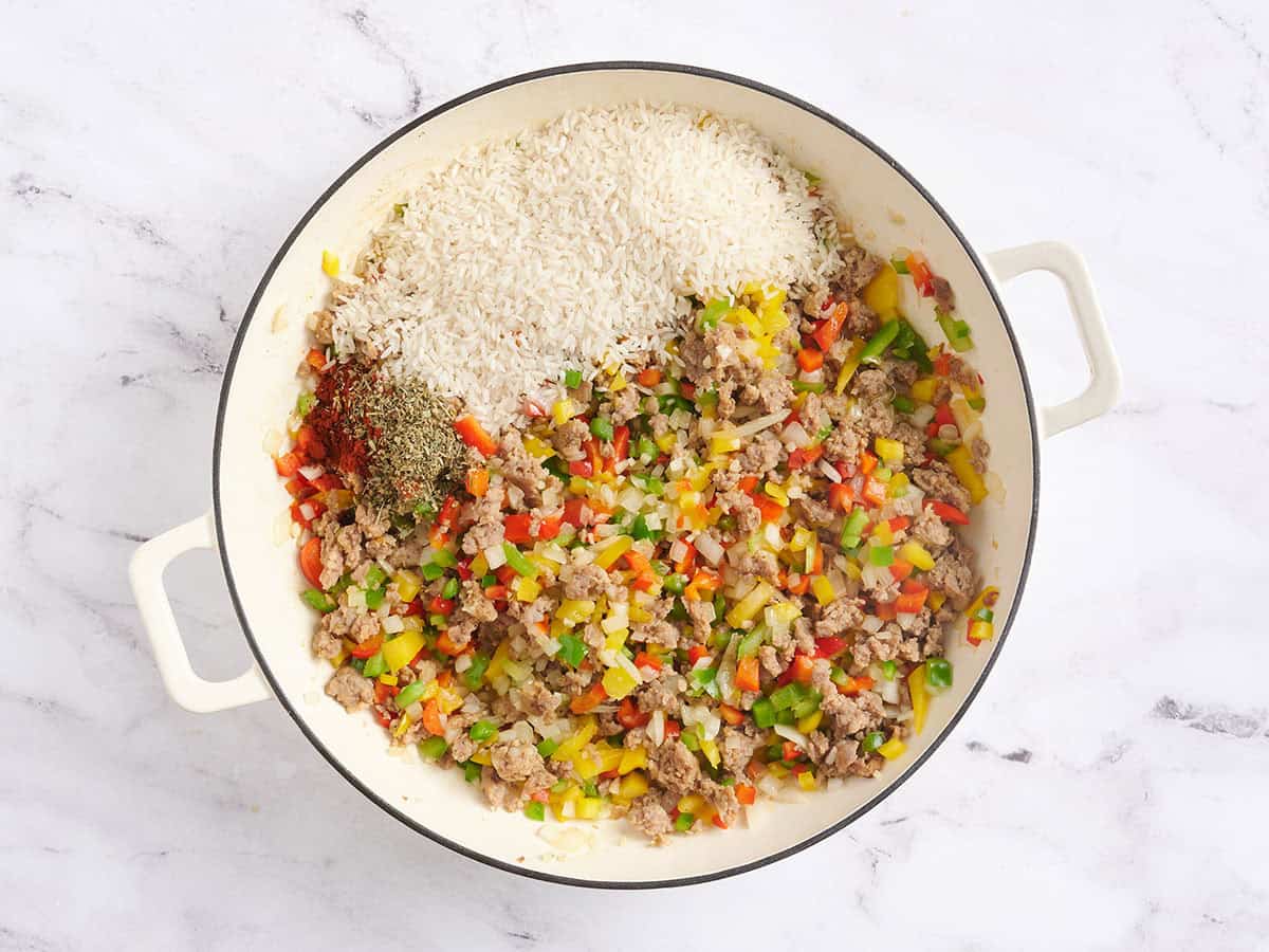 Riz et assaisonnements ajoutés à une poêle avec des légumes sautés.