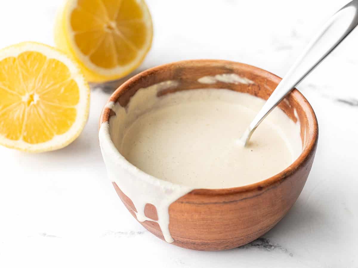 Vue latérale d'un bol en bois avec vinaigrette au tahini au citron, certains dégoulinant sur le côté