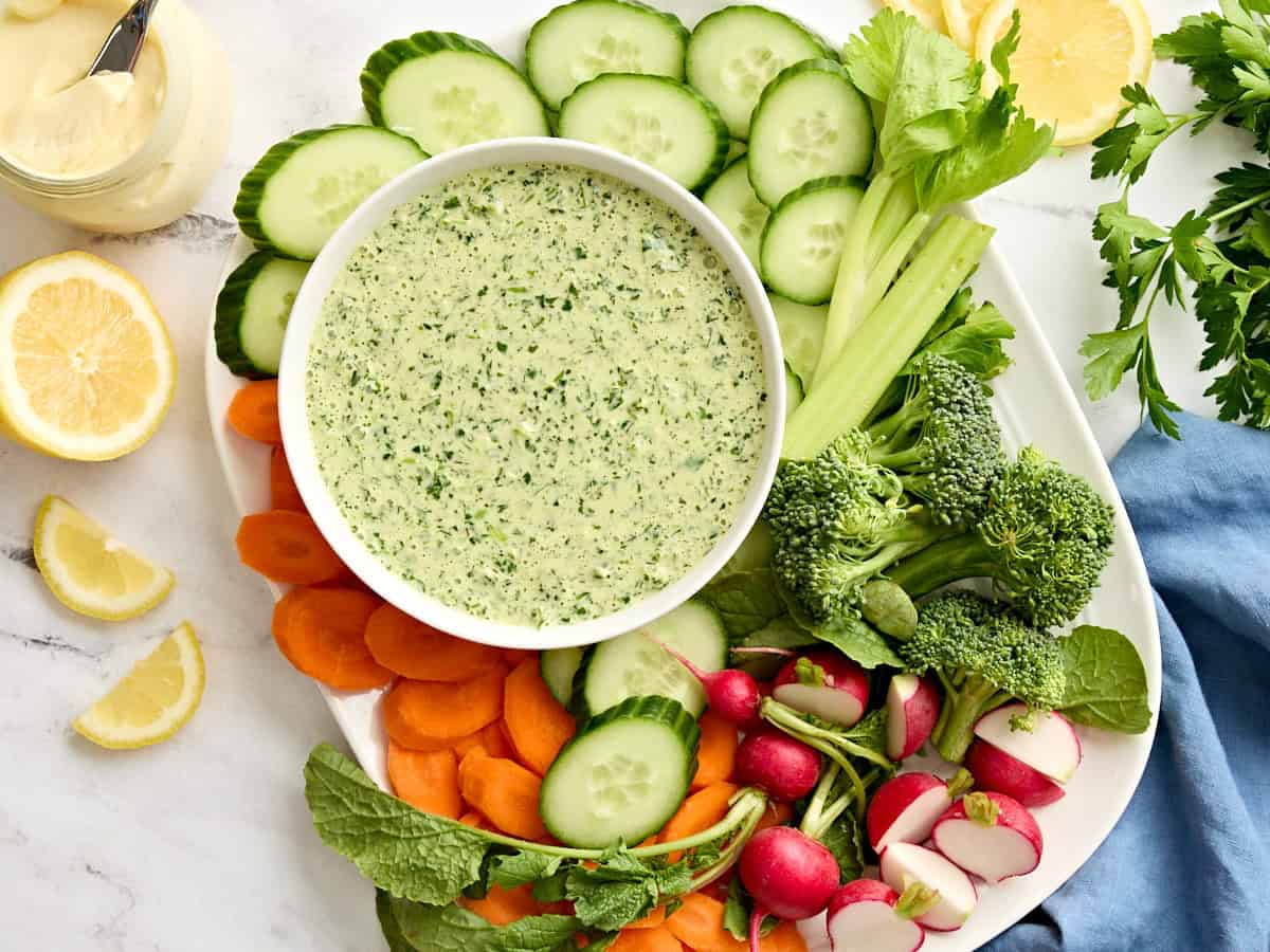 Vue aérienne d'un bol de vinaigrette déesse verte avec une assiette de légumes frais coupés.
