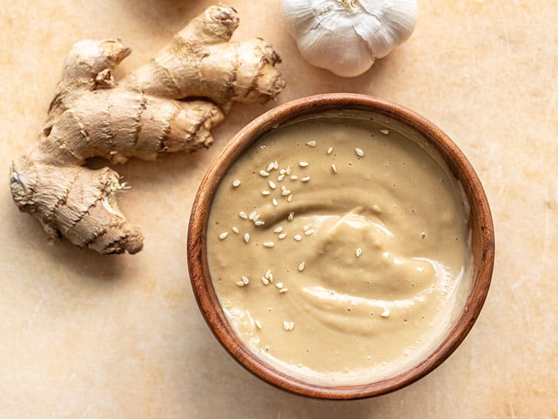 Un bol en bois rempli de vinaigrette sésame-gingembre à côté d'une noix de gingembre frais