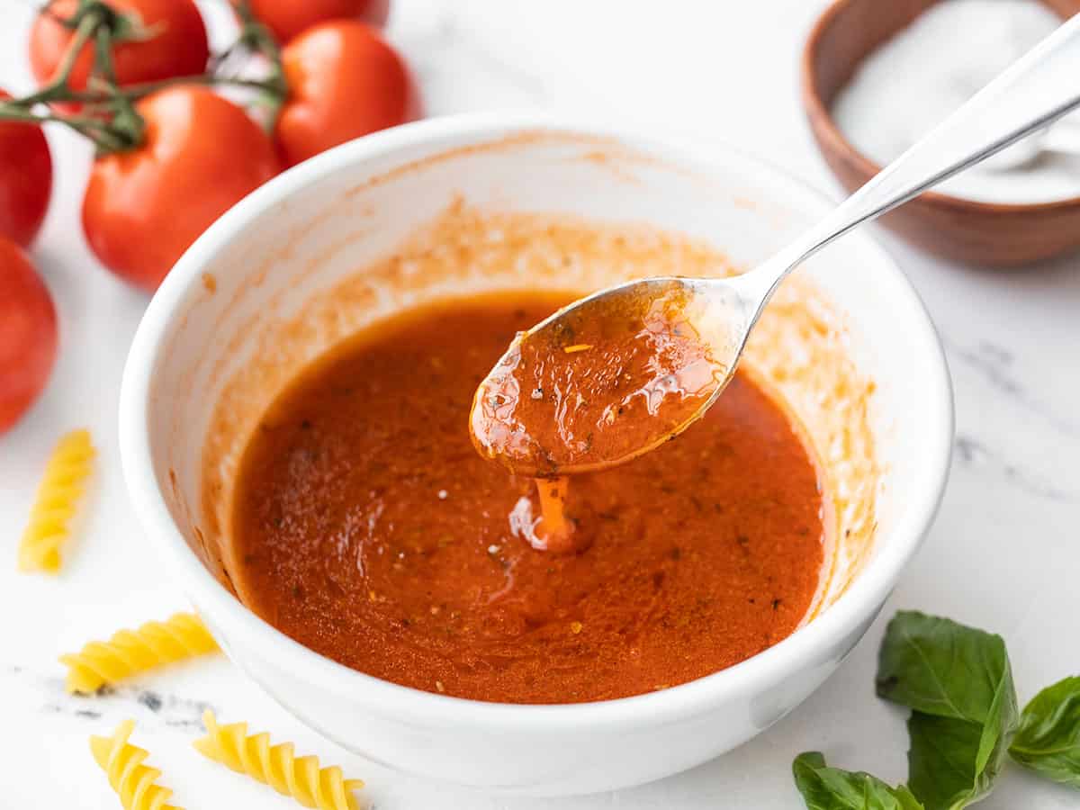 Vue latérale d'un bol de vinaigrette tomate basilic avec une cuillère dégoulinant de vinaigrette dans un bol