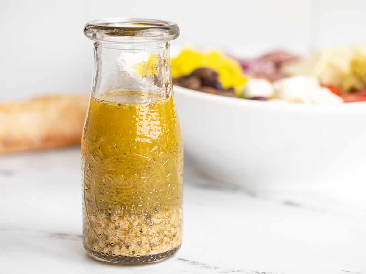 Vinaigrette italienne dans une carafe en verre devant un bol de salade