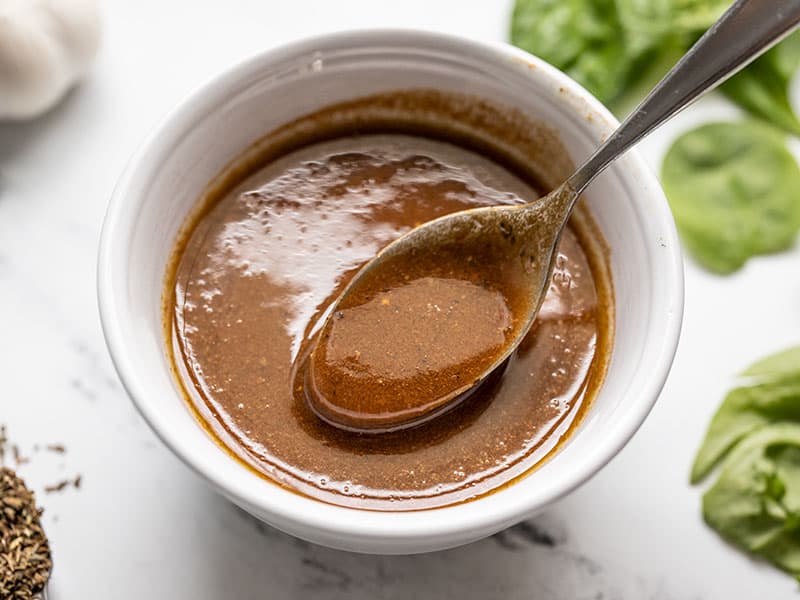 Une cuillère soulevant un peu de vinaigrette balsamique maison dans un petit bol