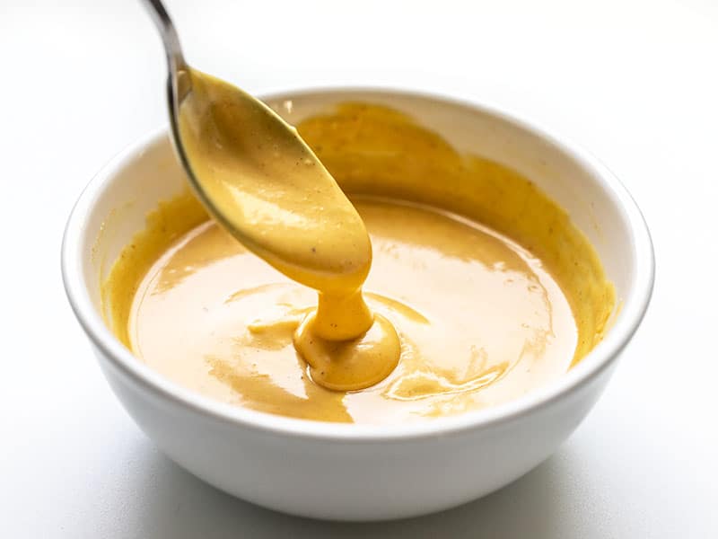 Sauce moutarde au miel dégoulinant d'une cuillère dans un bol