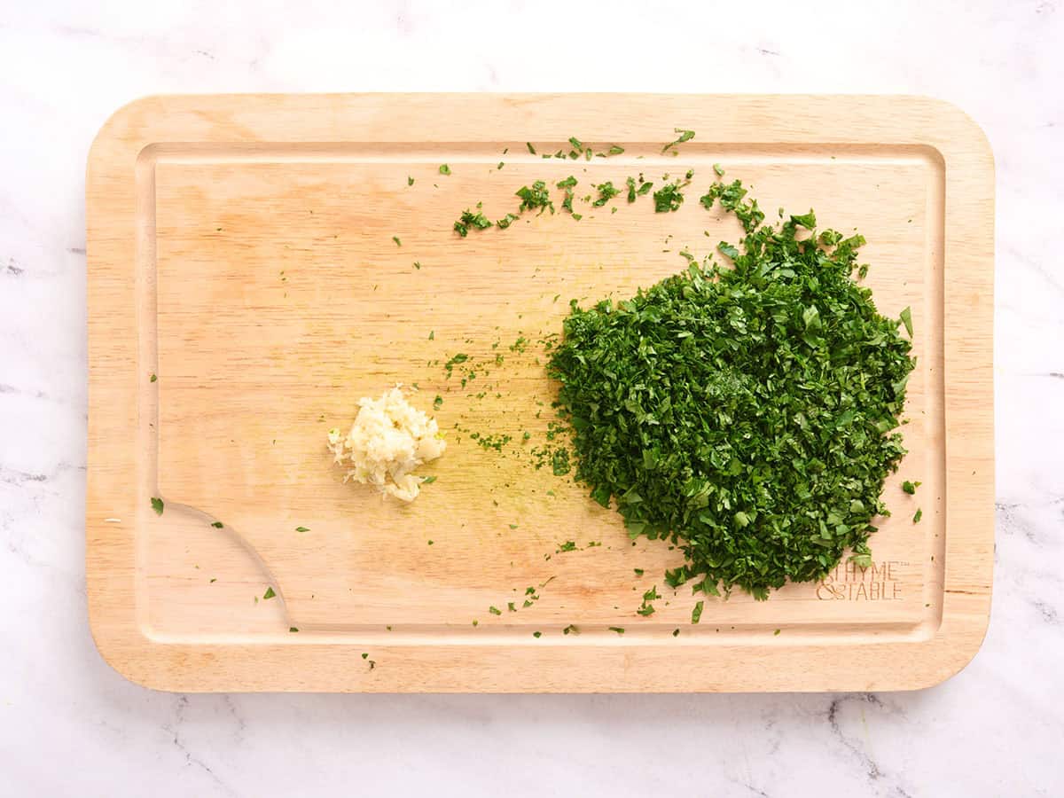 Herbes hachées et ail émincé sur une planche à découper.