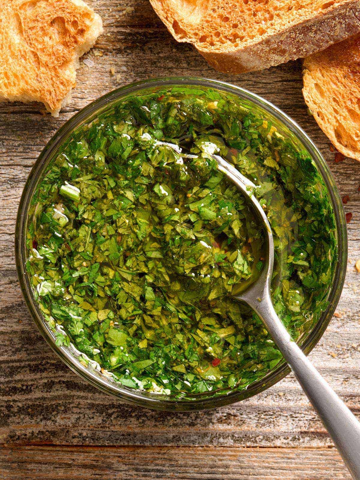 La sauce chimichurri est une sauce piquante, fraîche et à l'ail qui donne une grande saveur à n'importe quel repas. Utiliser comme marinade, trempette ou condiment. Budgetbytes.com Vue aérienne d'un bol de sauce chimichurri avec une cuillère.