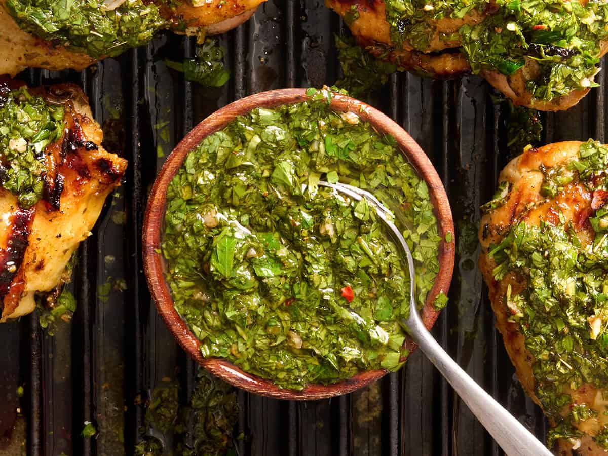 Vue aérienne d'un bol de chimichurri sur un grill avec une cuillère et des cuisses de poulet grillées.