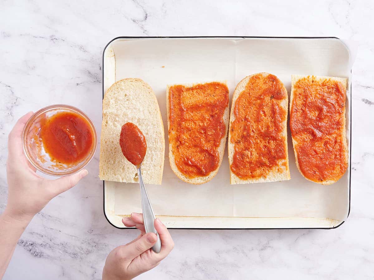 Verser à la main la sauce à pizza sur des quartiers de pain français.