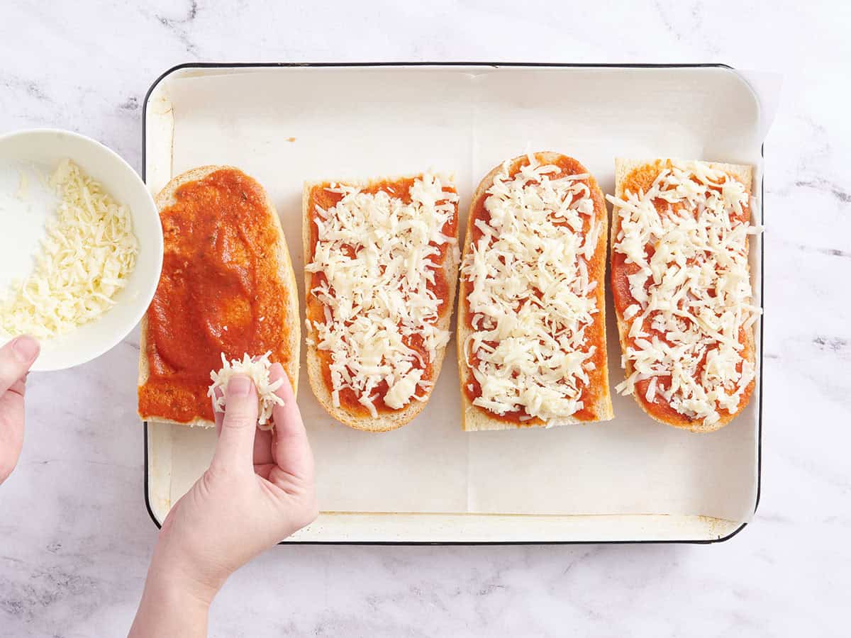 Une main saupoudrant du fromage râpé sur des pizzas au pain français.