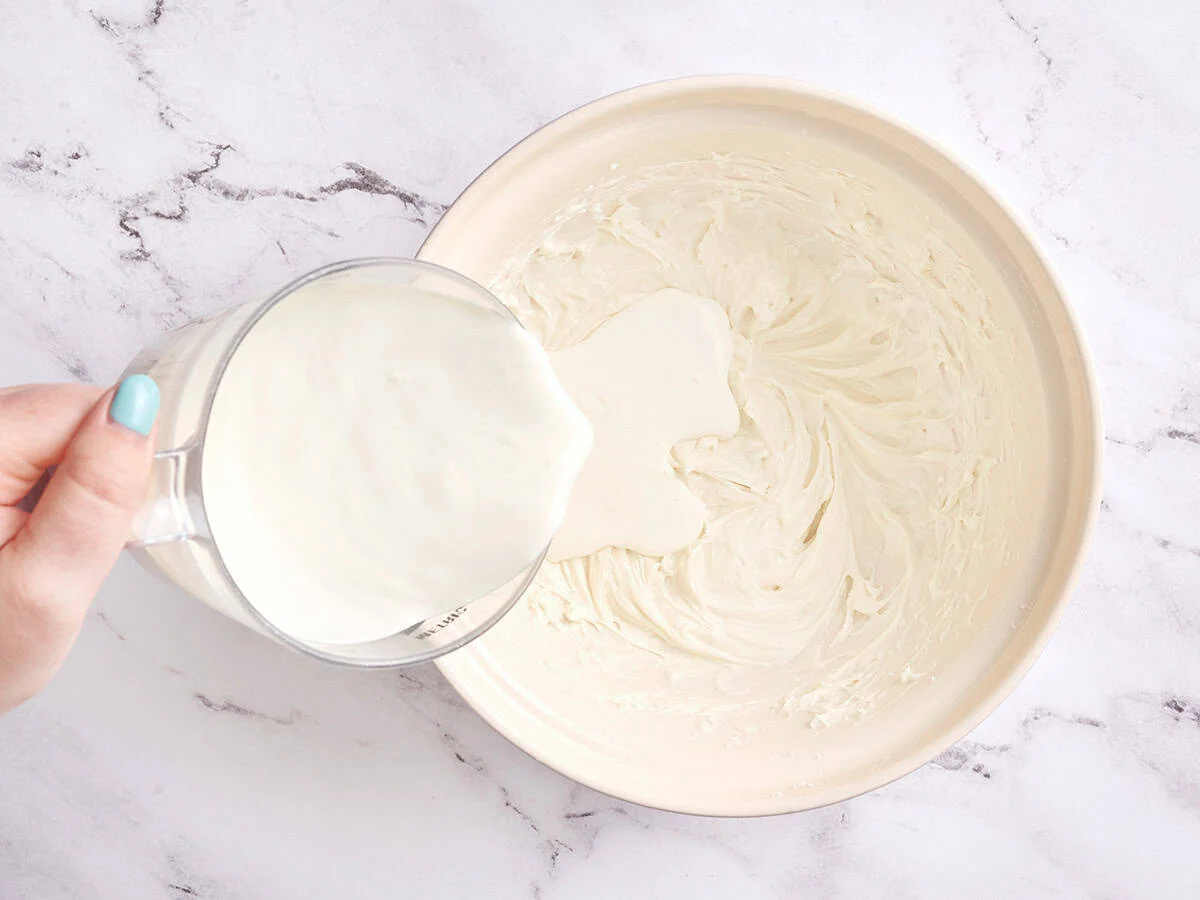 Crème versée dans du fromage à la crème fouetté.