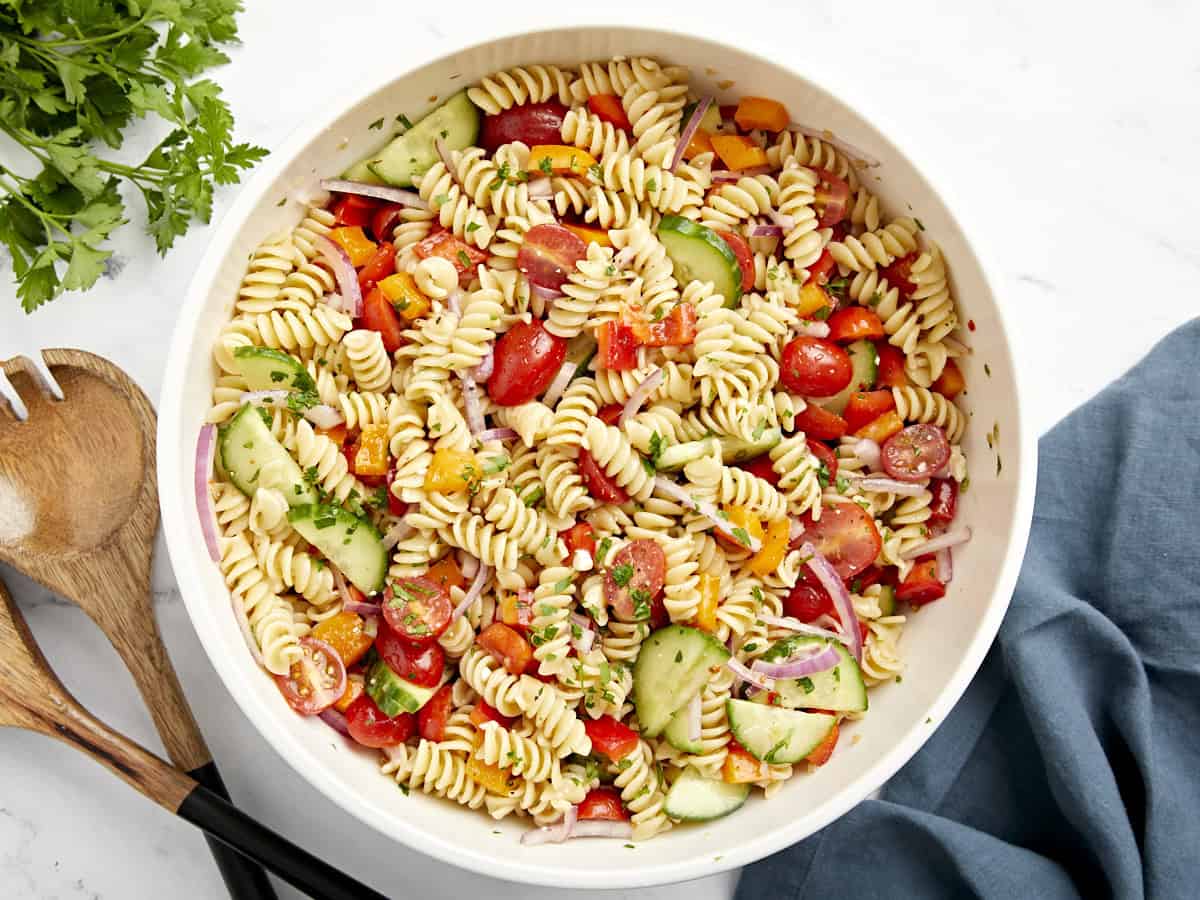 Vue aérienne de la salade de pâtes dans un grand bol de service blanc avec des ustensiles de service en bois sur le côté.