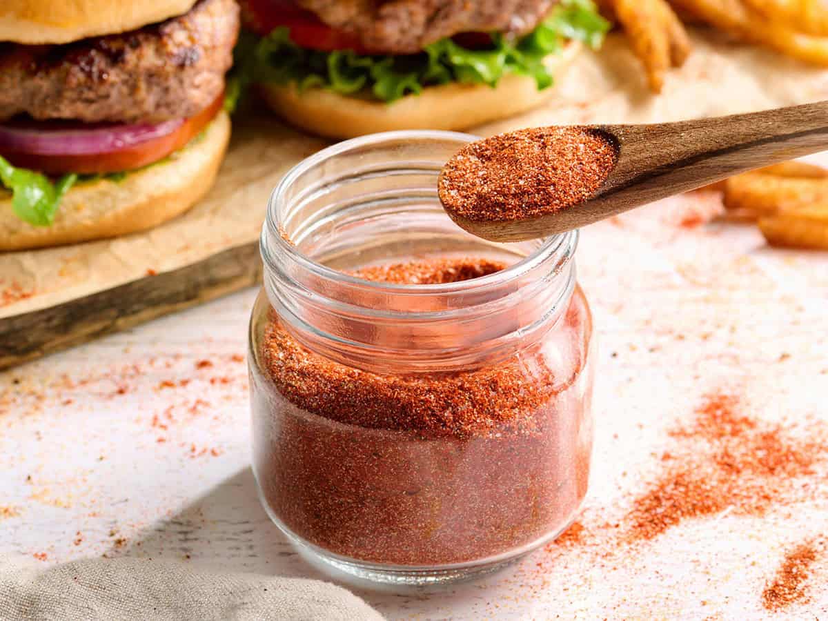 Side view of homemade burger seasoning in a jar with a spoon.