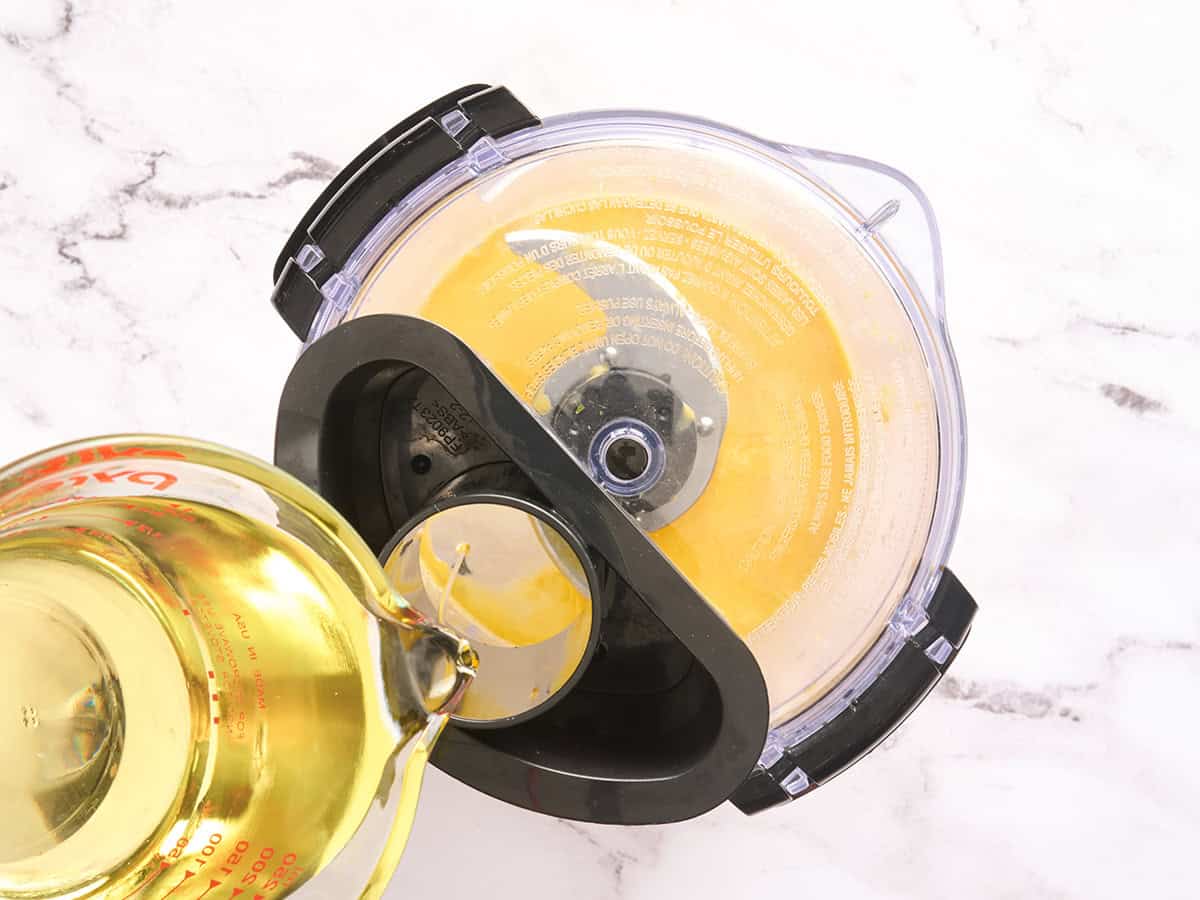 L'huile est versée dans un robot culinaire pour faire une émulsion pour l'aïoli à l'ail.