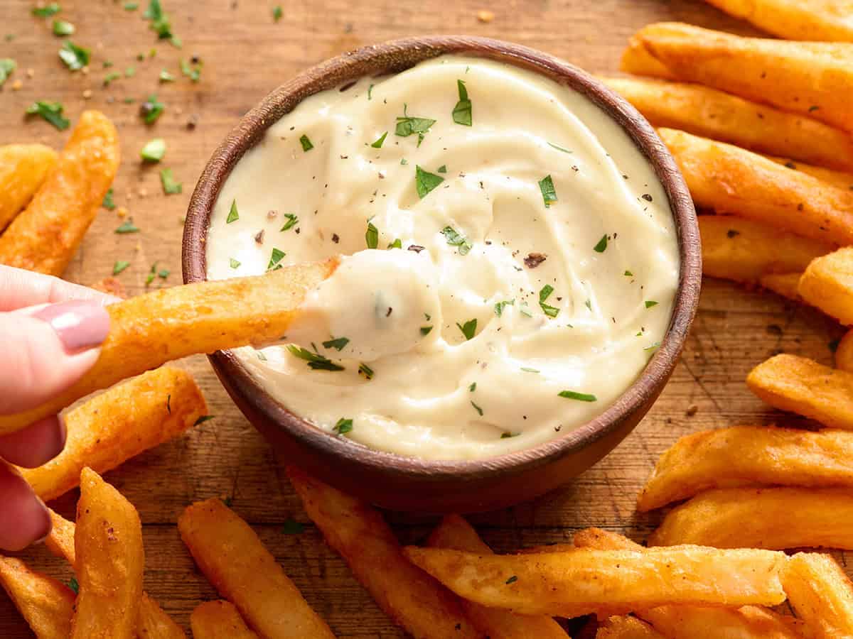 Vue latérale aérienne d'un bol d'aïoli à l'ail fait maison dans lequel on trempe une frite.