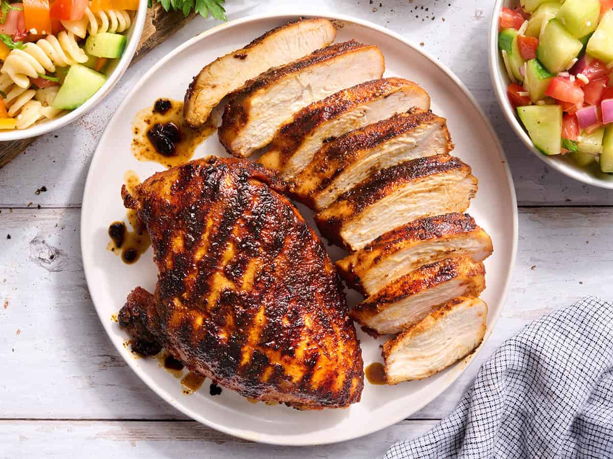 Vue aérienne d'une poitrine de poulet grillée sur une assiette avec une autre poitrine coupée en tranches.