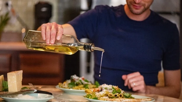 homme versant de l'huile d'olive sur son dîner