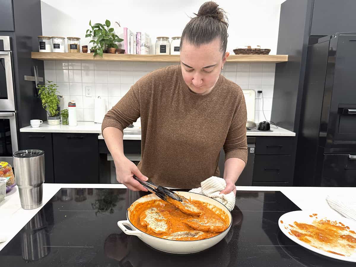 Une femme prépare du poulet crémeux aux tomates dans une poêle.