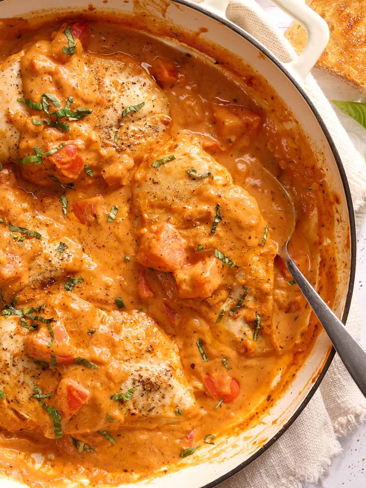 Vue aérienne d'une poêle de poulet crémeux aux tomates avec une cuillère.