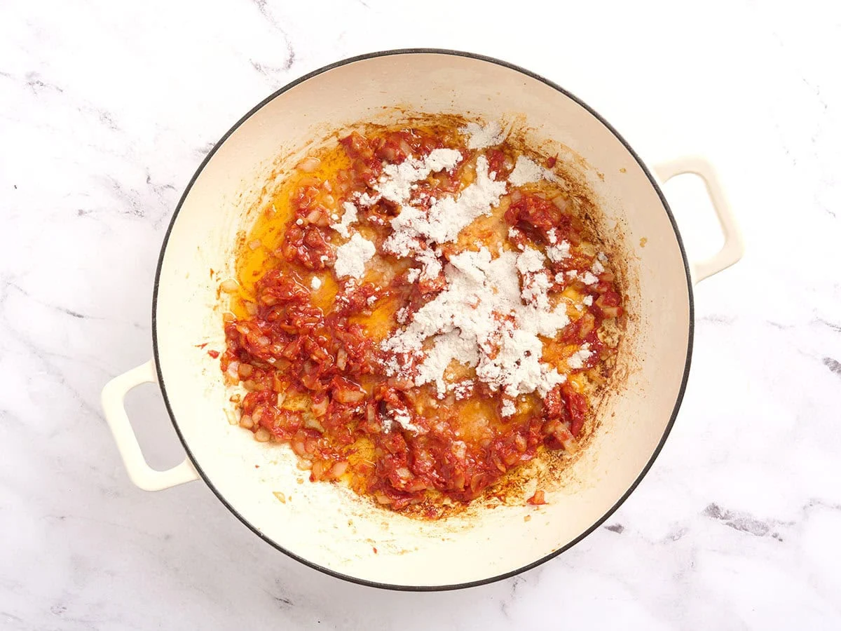 Farine ajoutée dans une poêle avec des oignons tomates pour faire un roux.