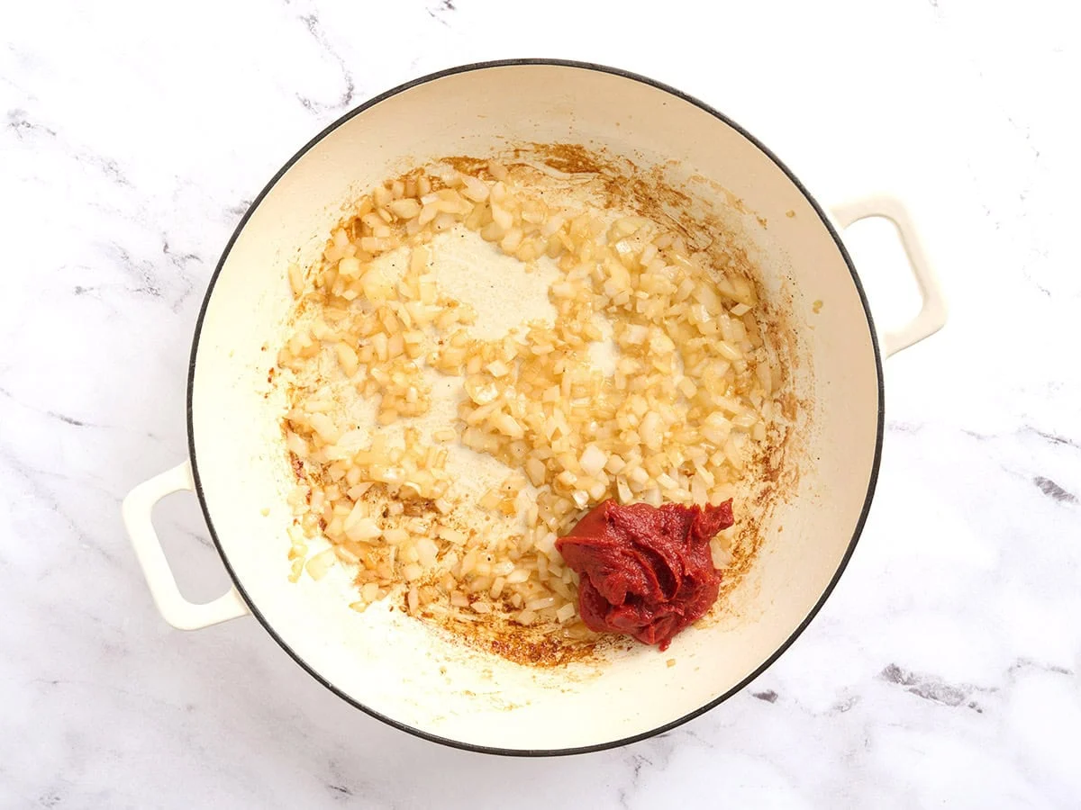 Pâte de tomate ajoutée dans une poêle sur les oignons et l'ail sautés.