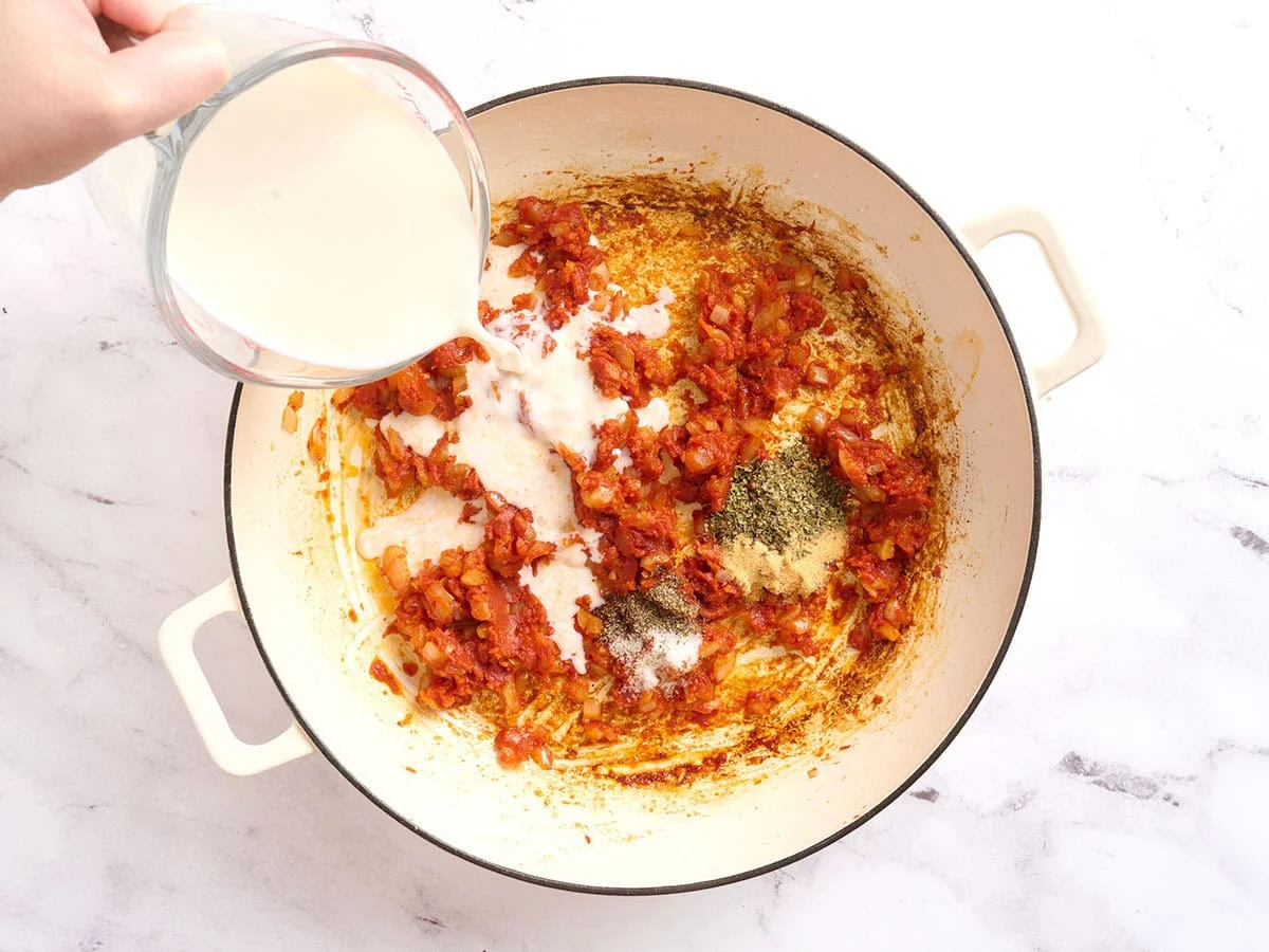 Le lait est versé dans une poêle pour faire une sauce tomate crémeuse.