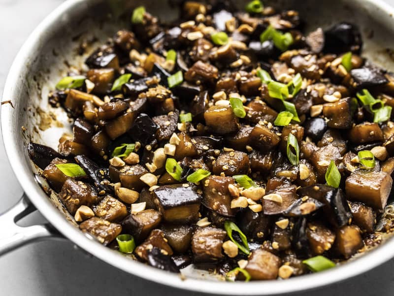 Vue rapprochée de l'aubergine glacée au soja dans la poêle, garnie d'arachides et d'oignon vert