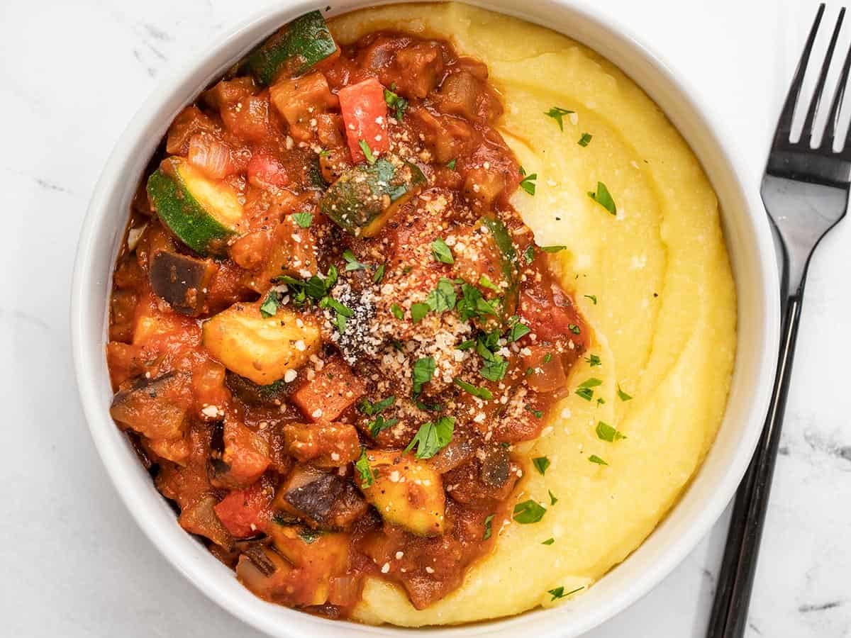 Vue rapprochée de la semoule de maïs et des légumes en sauce rouge dans un bol avec une fourchette sur le côté.