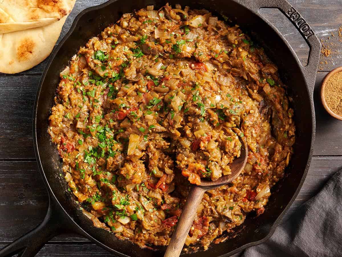 Vue aérienne du curry d'aubergines dans une poêle avec une cuillère en bois.