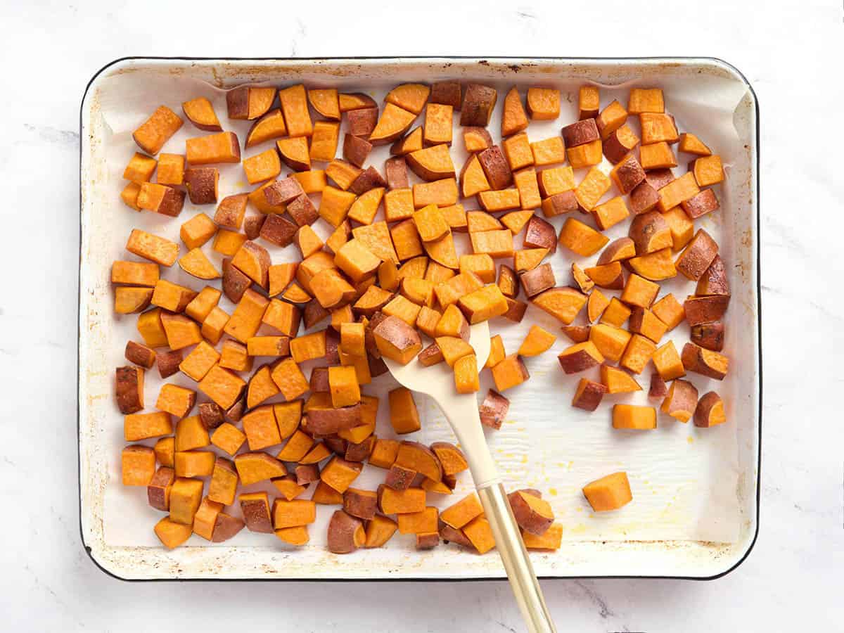 Cubes de patates douces sur une plaque à pâtisserie mélangés à une spatule.