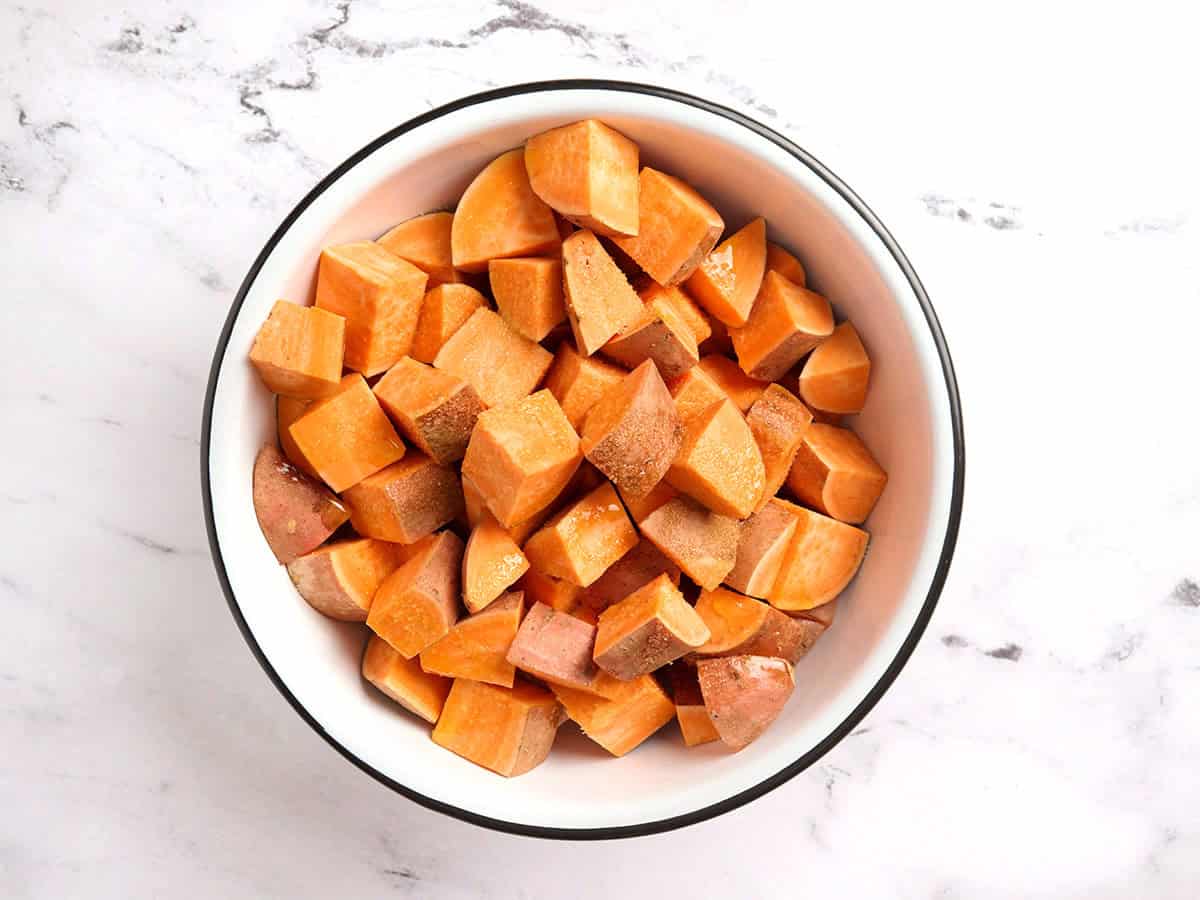 Patates douces coupées en dés dans un bol avec de l'huile et du sel.