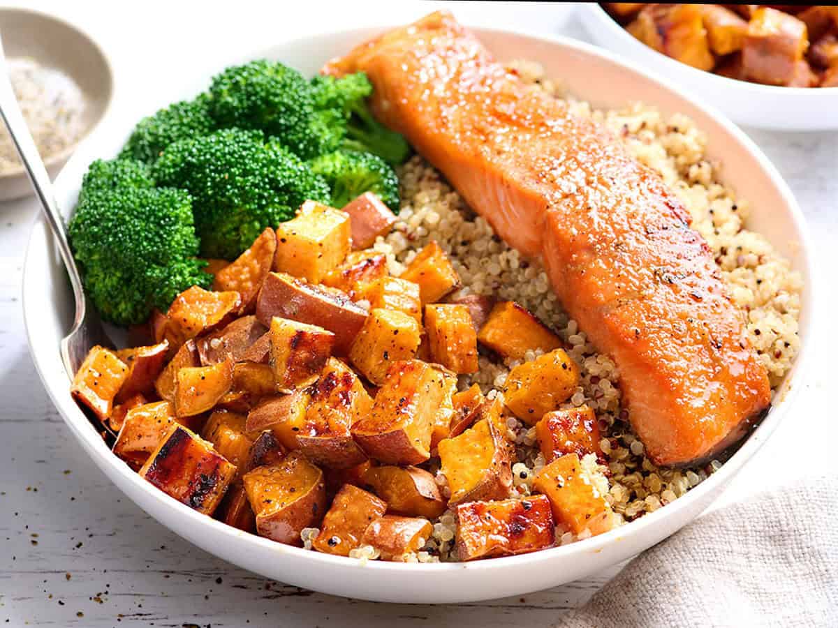 Vue de face d'un bol de quinoa avec un filet de saumon, des patates douces rôties et du brocoli.
