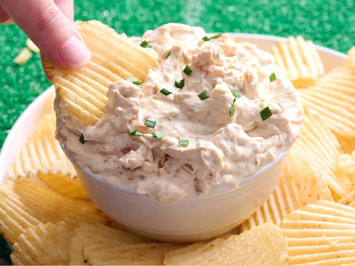 Une main trempant une chips dans une trempette à l'oignon française.