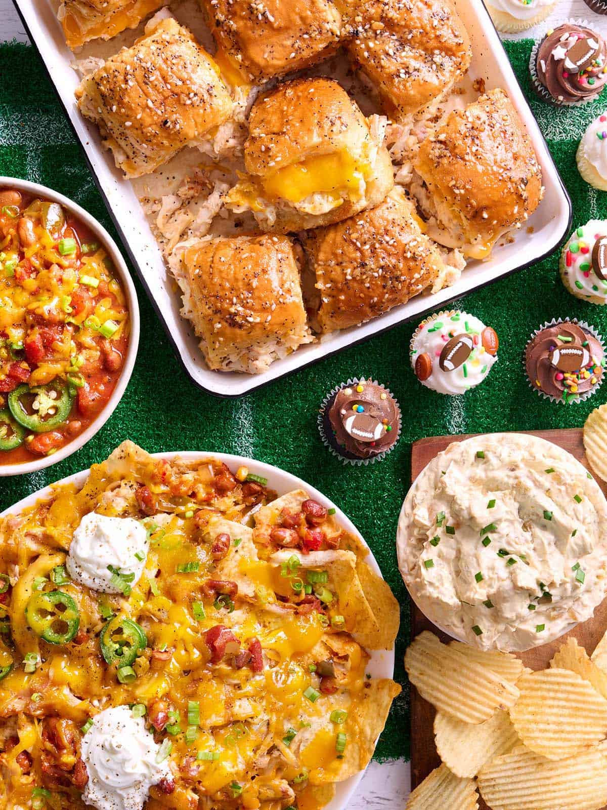 Vue aérienne d'une journée de match à tartiner, comprenant des sliders de poulet, du chili, des nachos, des trempettes et des cup cakes.