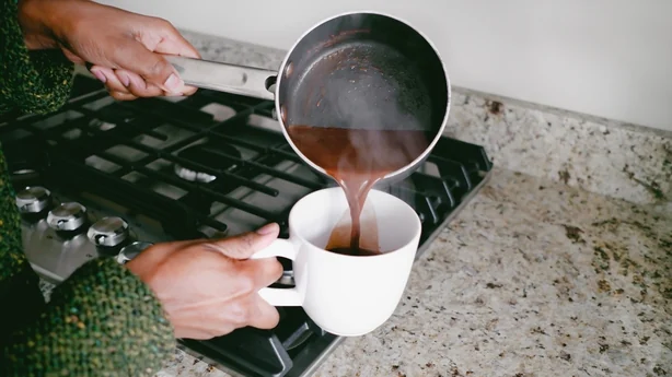 Gros plan d'une femme noire méconnaissable versant du chocolat chaud dans une tasse