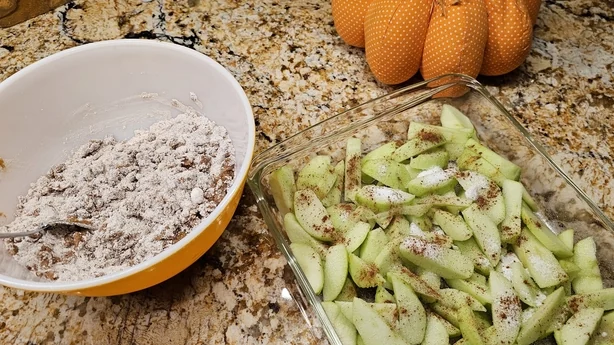 Tranches de pommes Granny Smith avec farine, muscade et cannelle dans un bol, prêtes à mélanger les ingrédients pour un délicieux dessert de saison préféré.